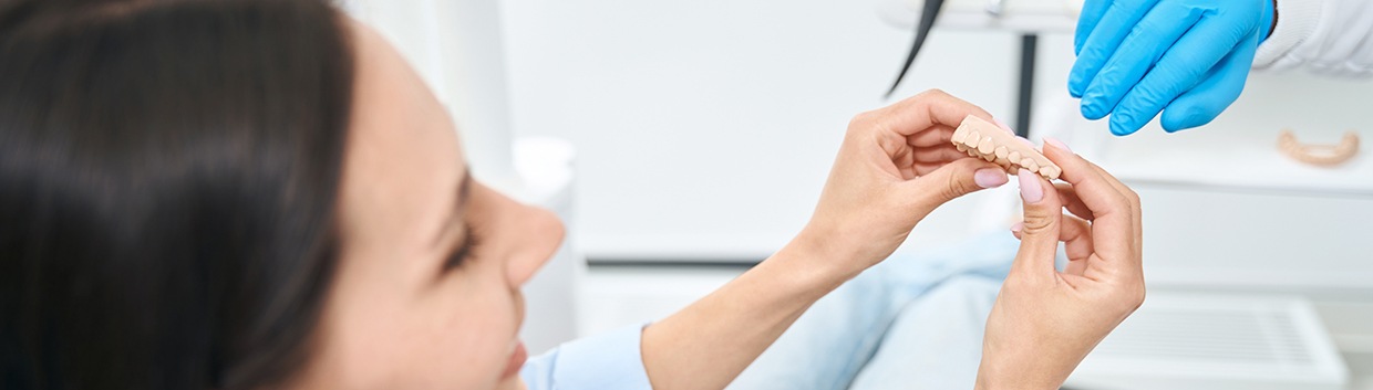 A curious woman holding a dental prosthetic
