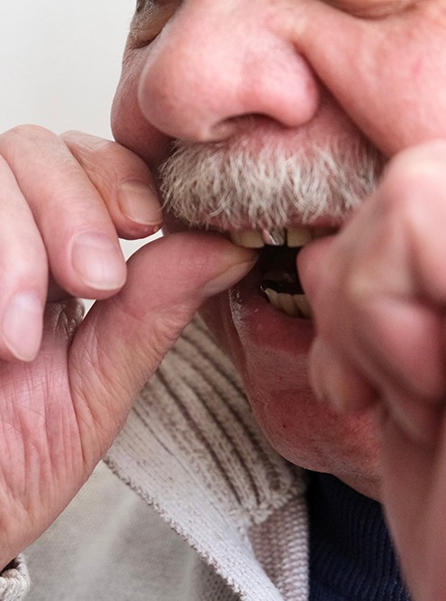 An older man putting dentures in his mouth
