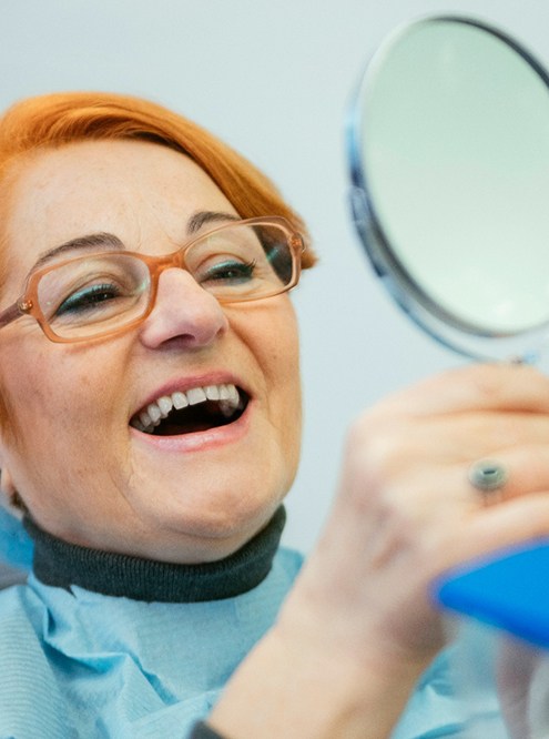 A senior woman admiring her restored smile with a hand mirror