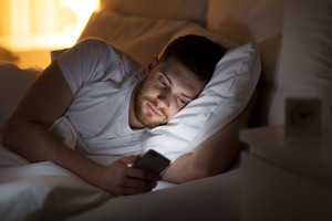 Man lying awake in bed and looking at his phone
